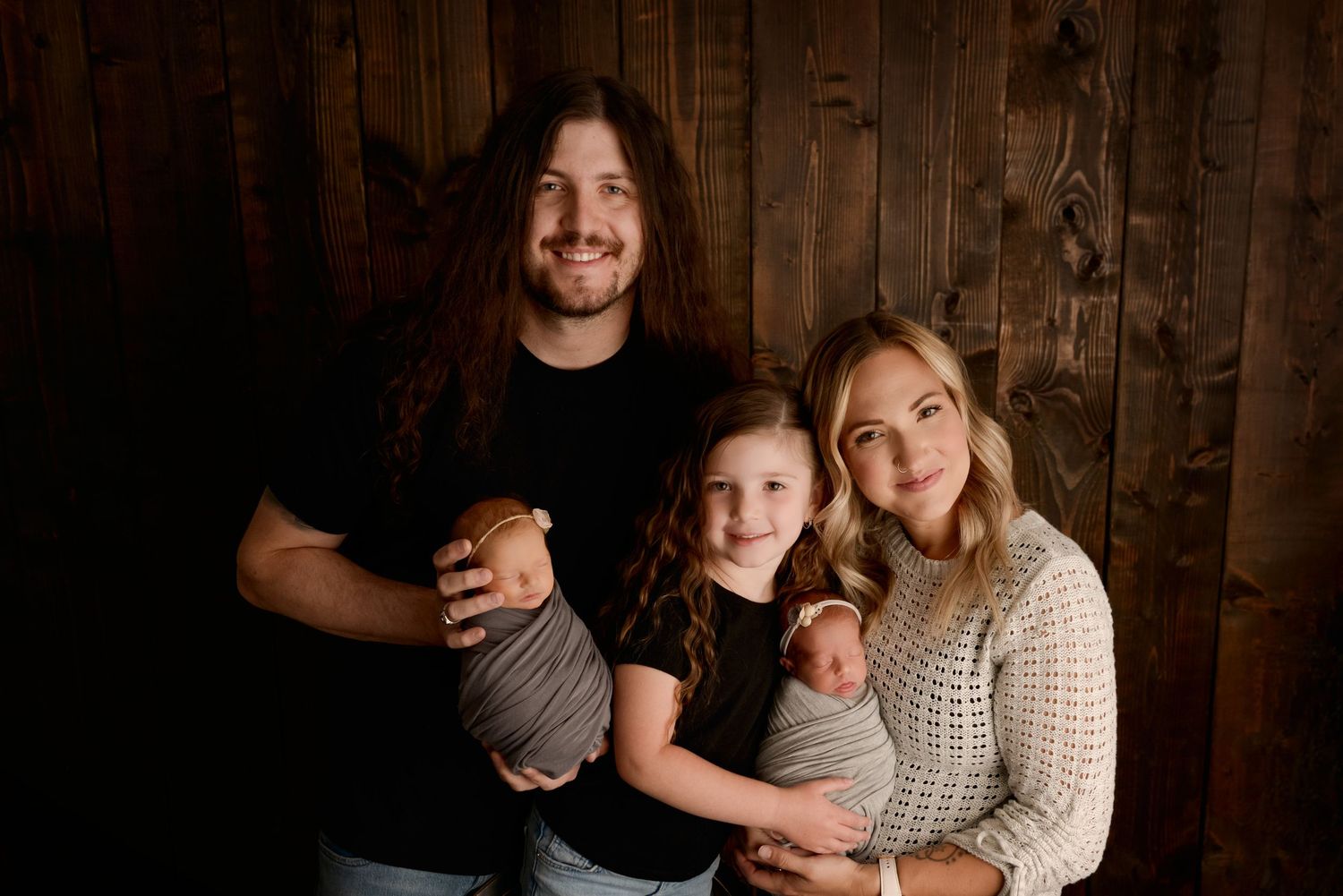 Intimate family photo session in dark wooden interior featuring affectionate poses and casual winter attire.