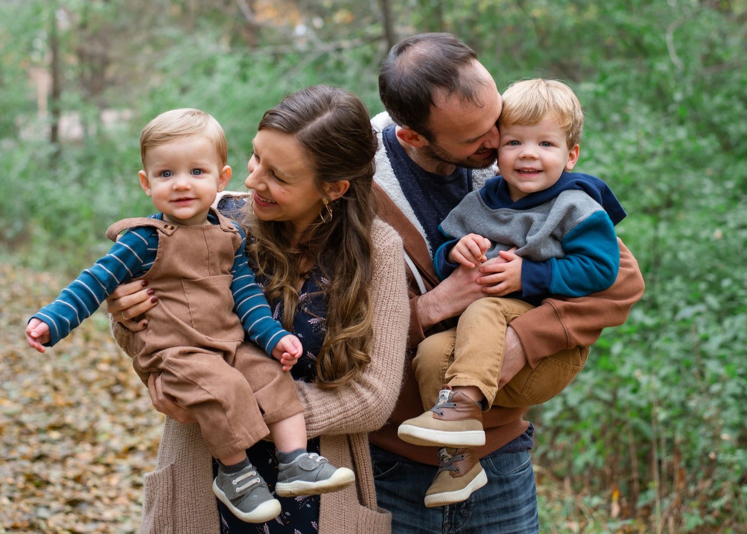 Family embraces and laughs together during an outdoor autumn photo session in a wooded forest setting.