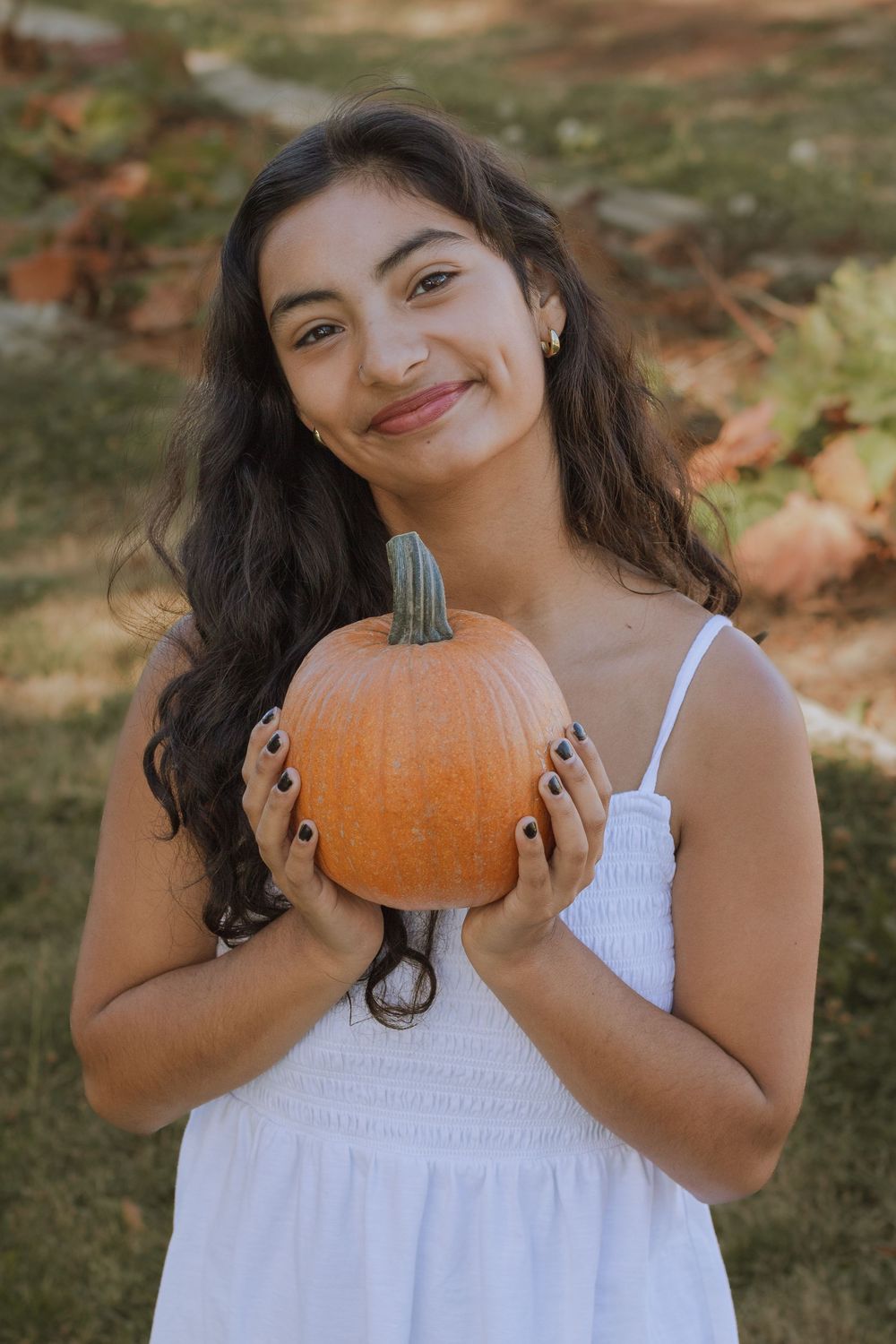 Girl posed with small orange pumpkin in hands.