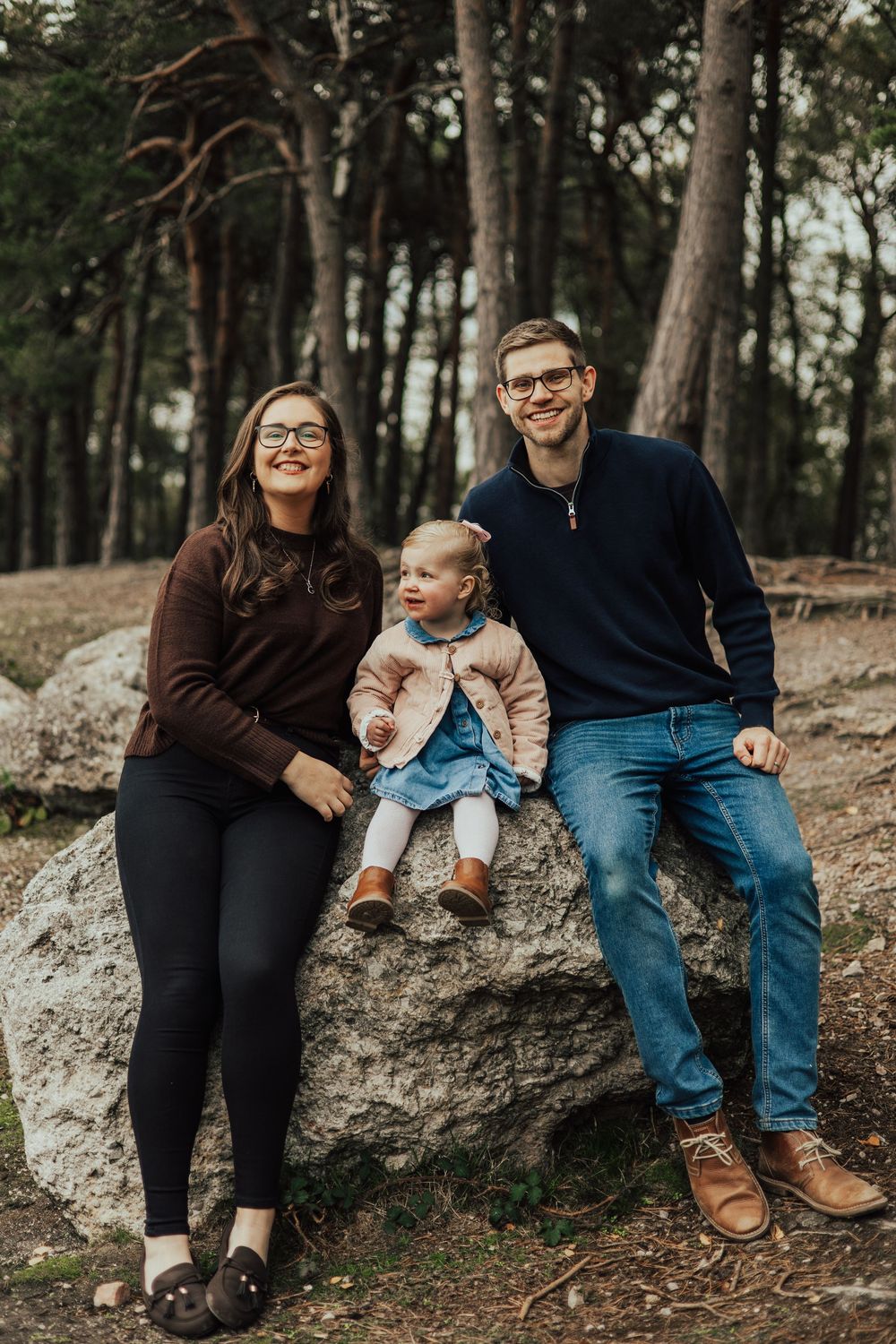 A family sits together on a large rock in a wooded forest setting, captured in a series of candid moments.