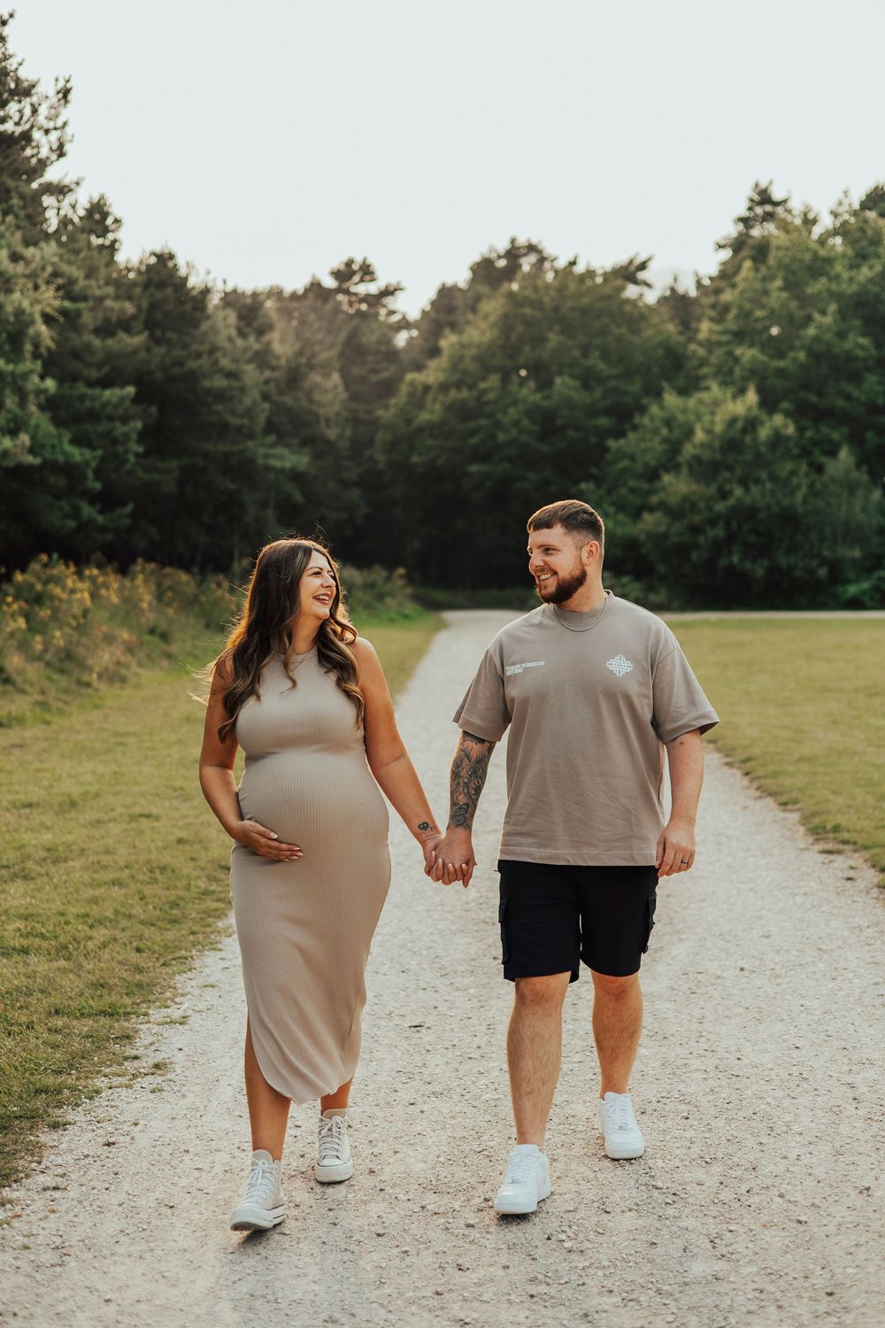 A couple walking hand in hand on a gravel path through a green park wearing casual summer outfits.