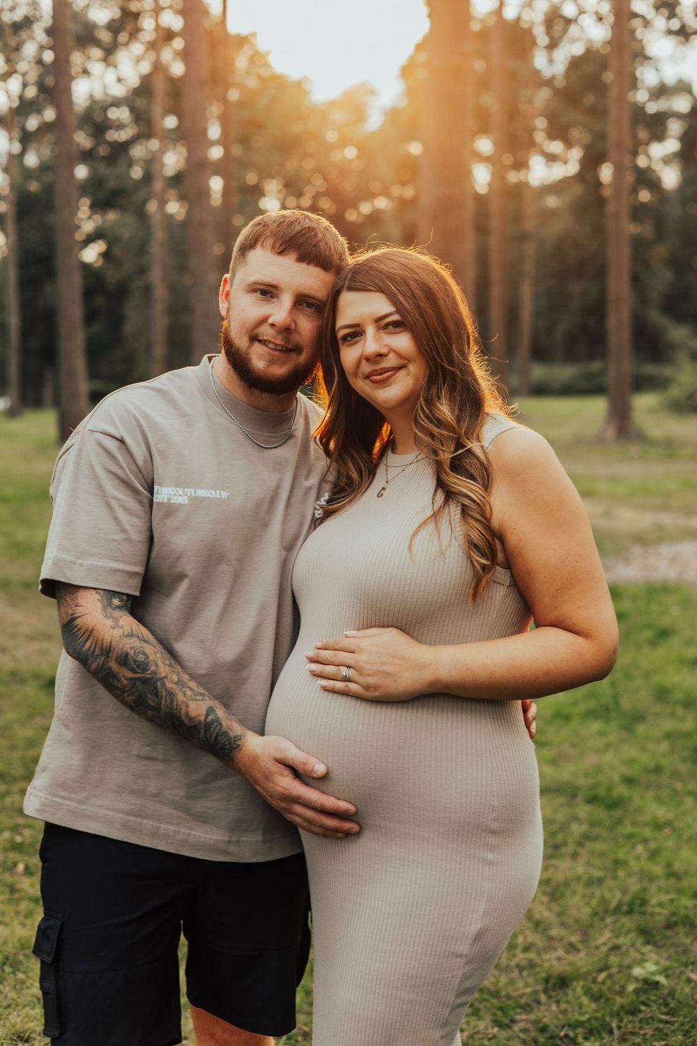 A couple embraces in a forest during golden hour sunset while taking maternity photos.