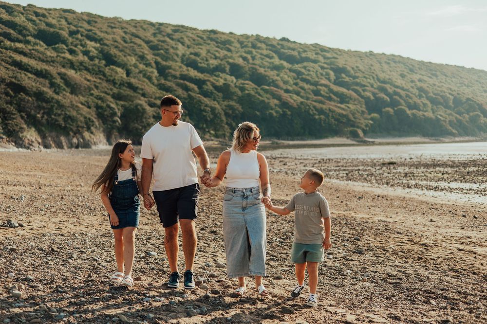 Family group walking together on a serene pebbled beach at sunset with hills in the background.