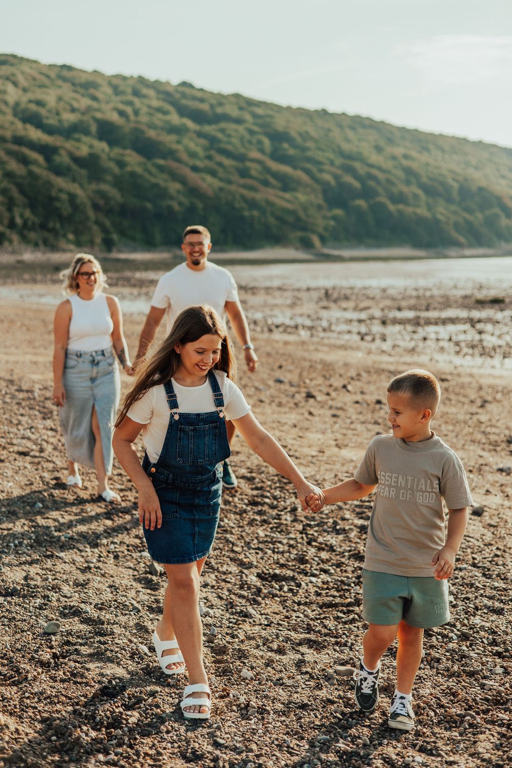 A group enjoys a relaxed sunny day walking along a rocky beach with coastal hills in the background at sunset.