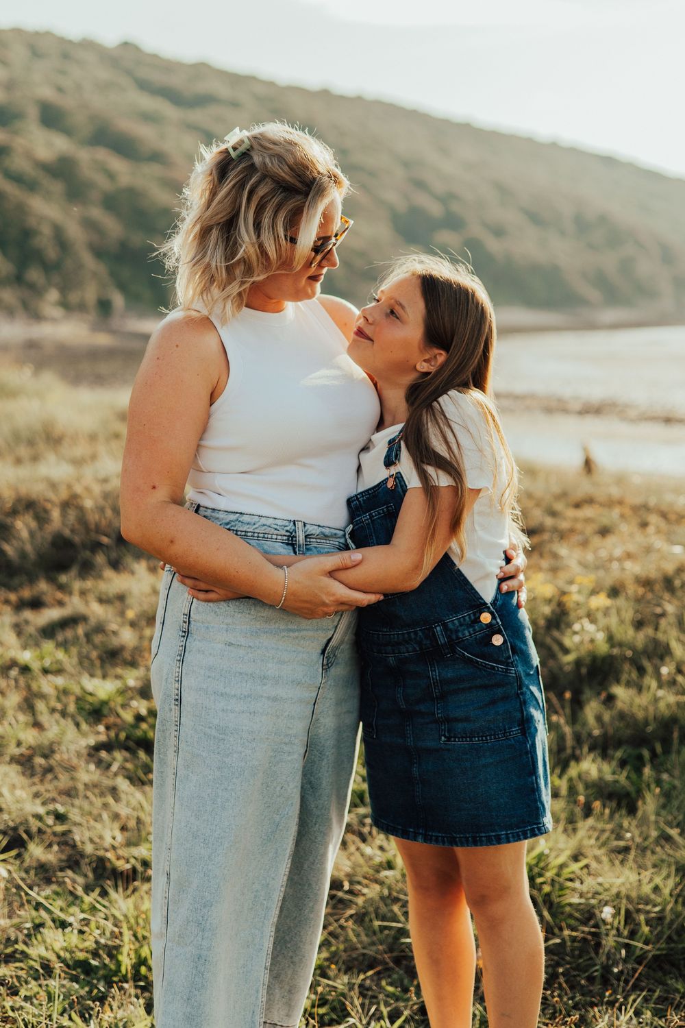 Candid outdoor portrait of parent and child embracing in golden sunlight near hillside lake.