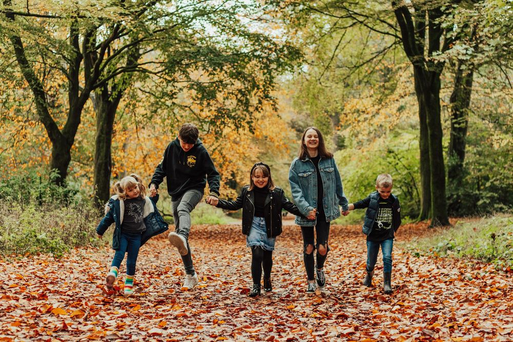A group walks together on a path covered in fallen autumn leaves surrounded by trees in a park.