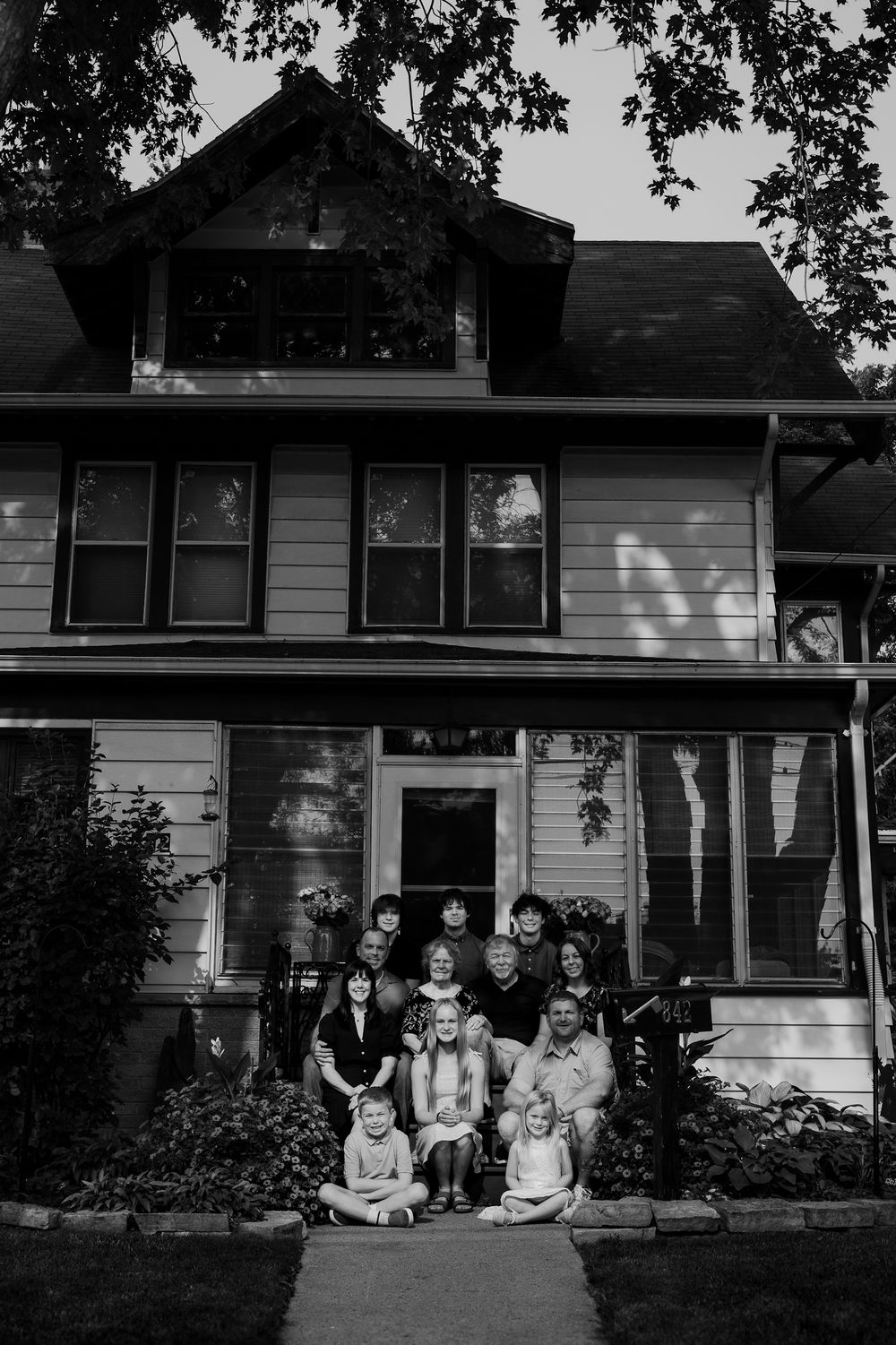Group of children sitting outdoors in front of white house in vintage black and white photograph.