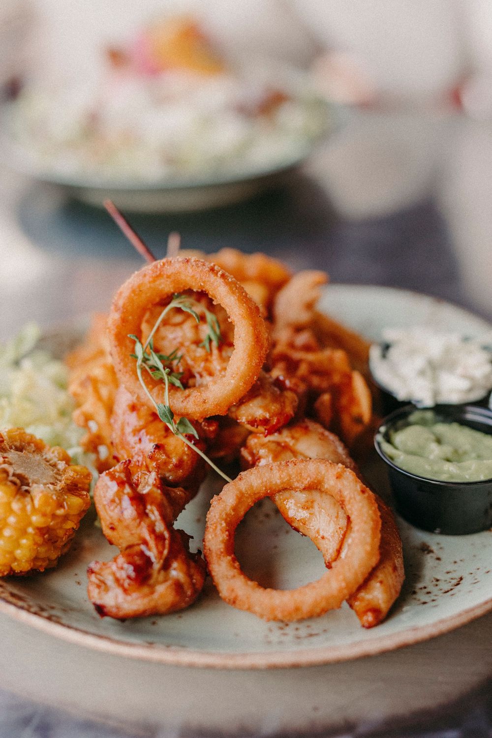 Crispy fried calamari rings served on a white plate with dipping sauce and fresh herbs.