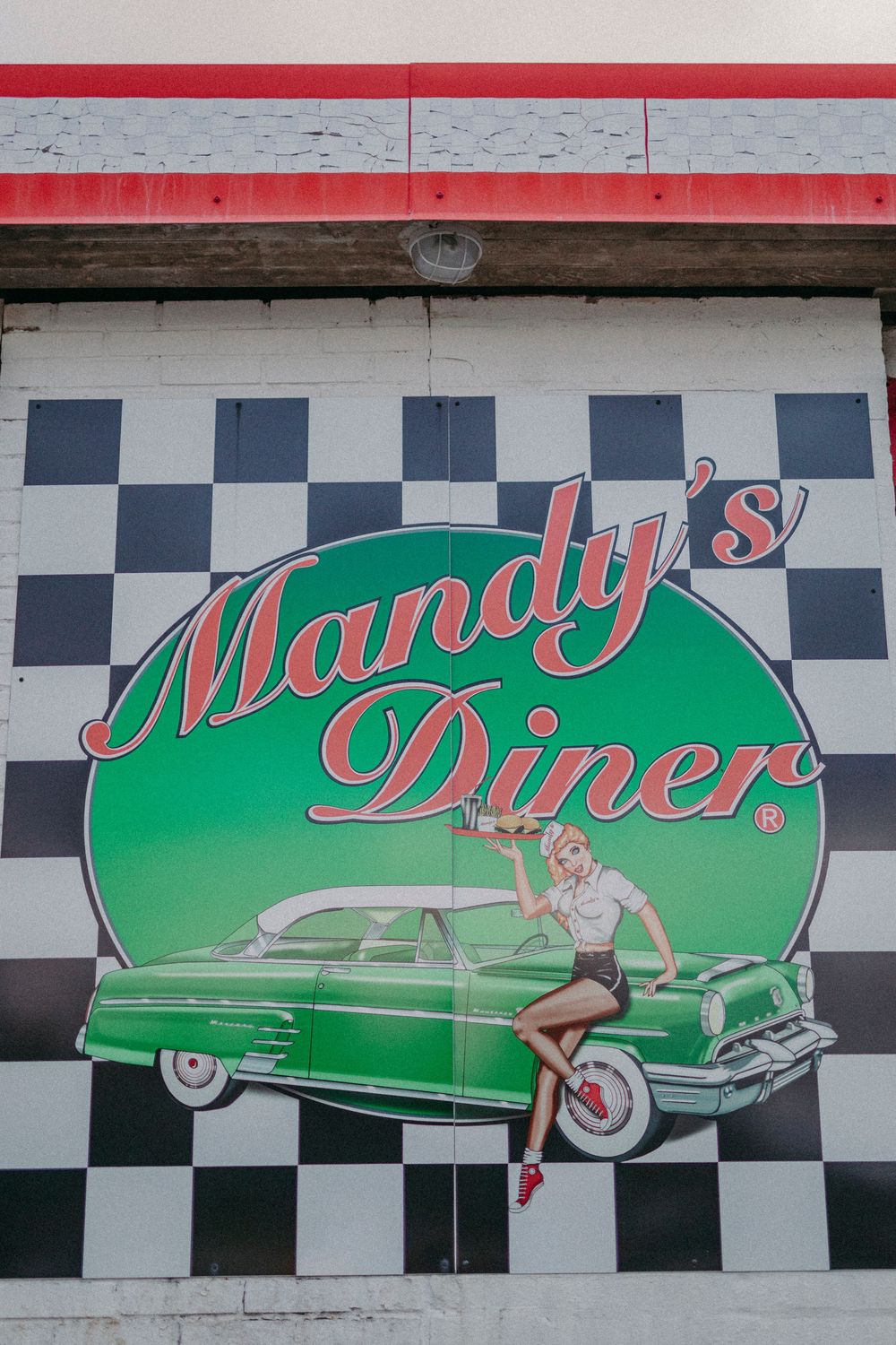 Vintage-style diner sign featuring a green car and retro imagery against a black and white checkered background.