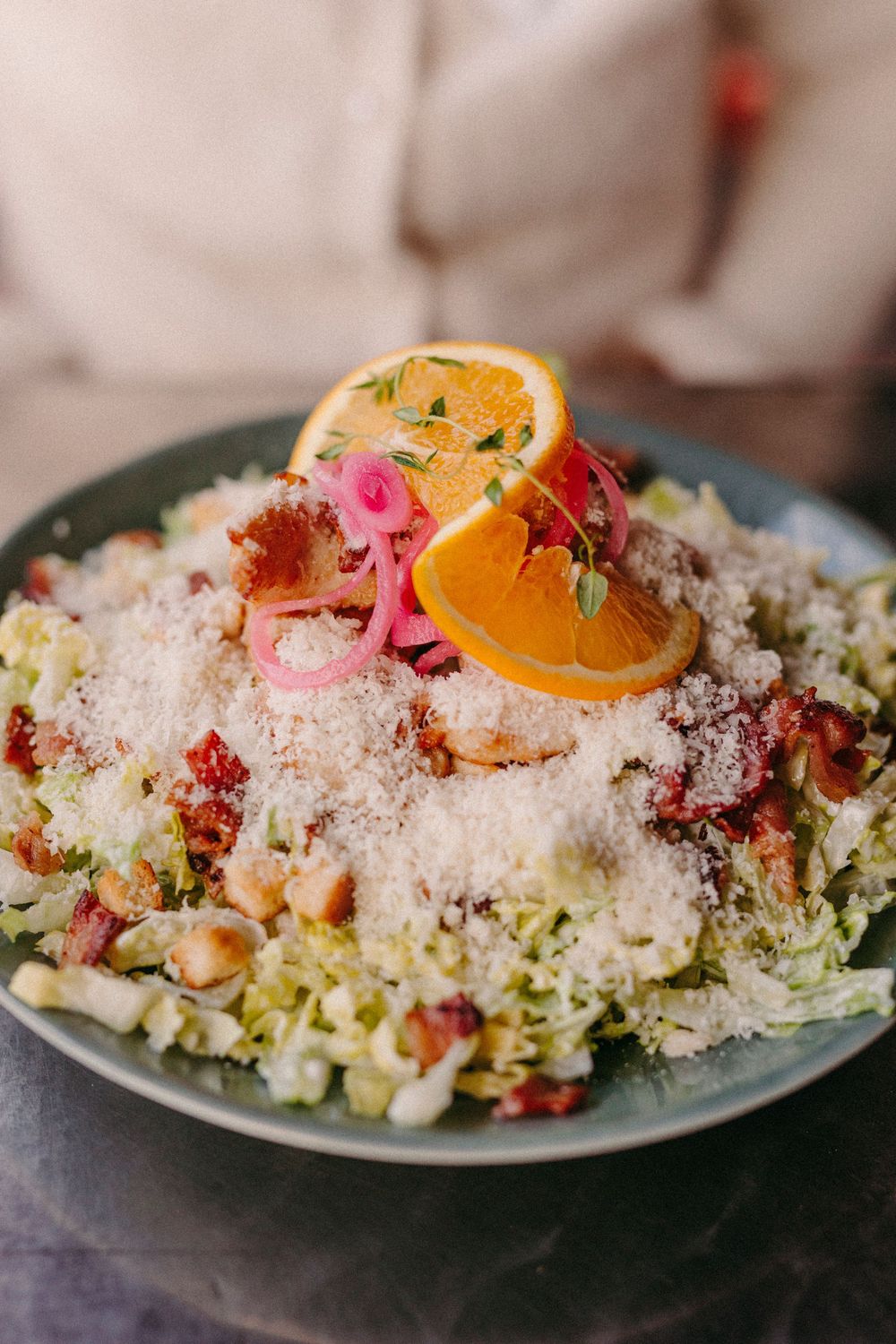 Colorful salad plate topped with shaved Parmesan cheese, pink pickled onions, and citrus slices.