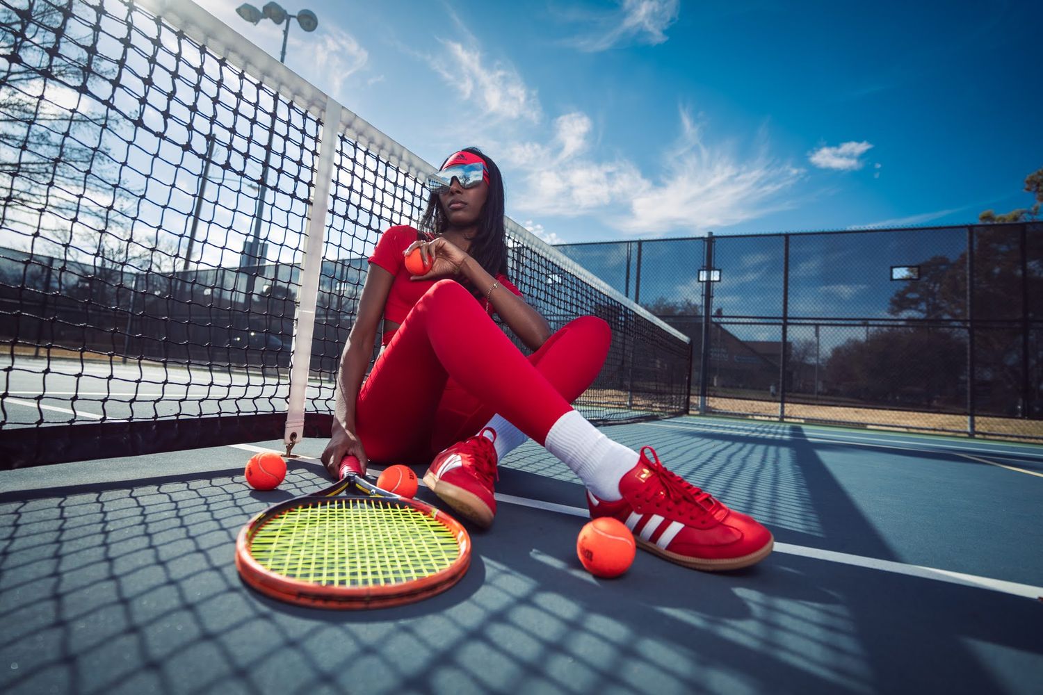 Close-up views of red tennis shoes on an outdoor tennis court with blue sky and net details visible in background.