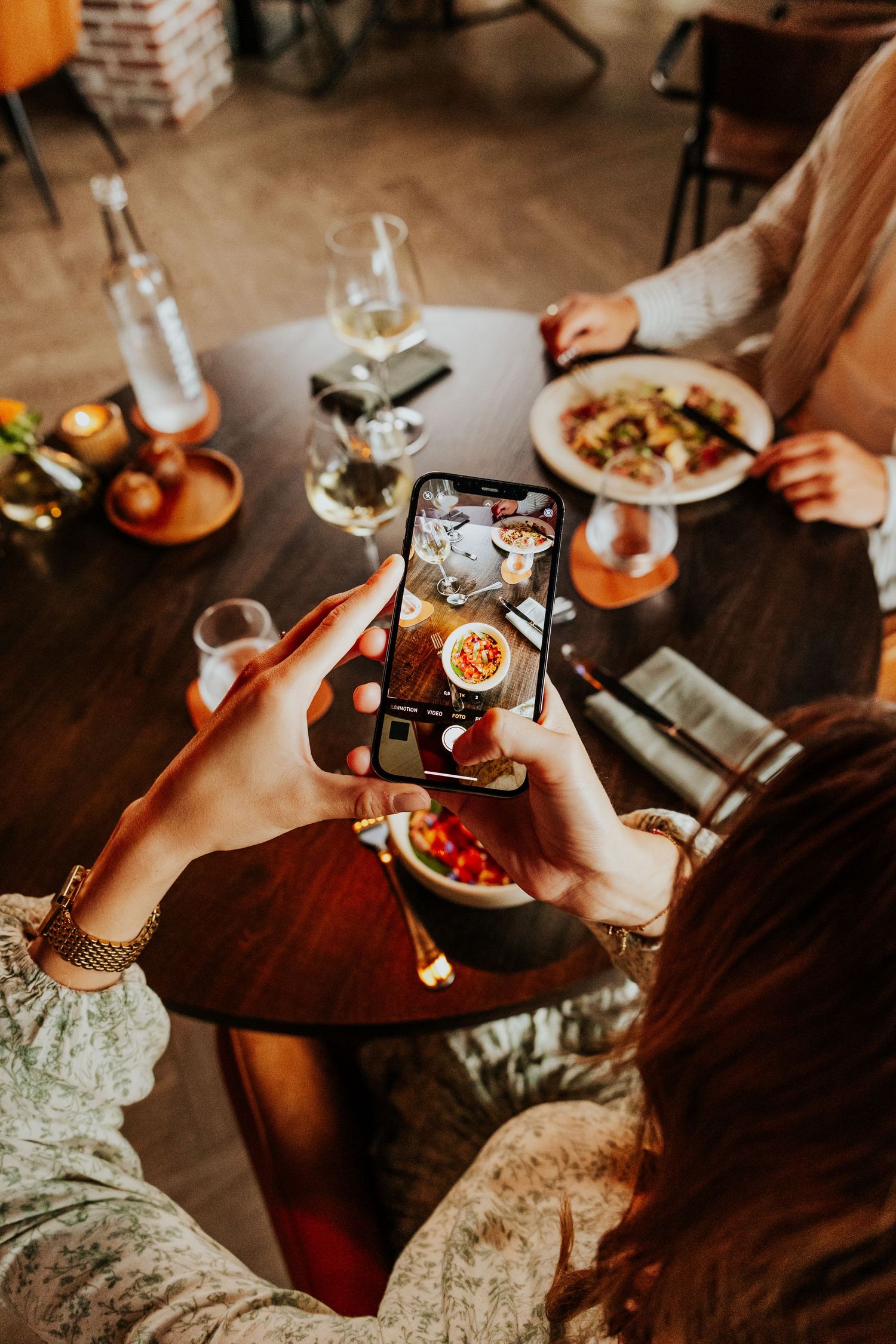 Overhead view of diners taking food photos with smartphones at a restaurant table.