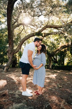 A couple shares tender moments in a sunlit wooded area during their engagement photo session in nature.