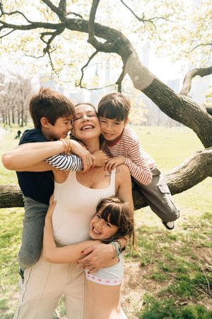 Four candid photos of family members embracing and sharing joyful moments together under a tree in a park setting.