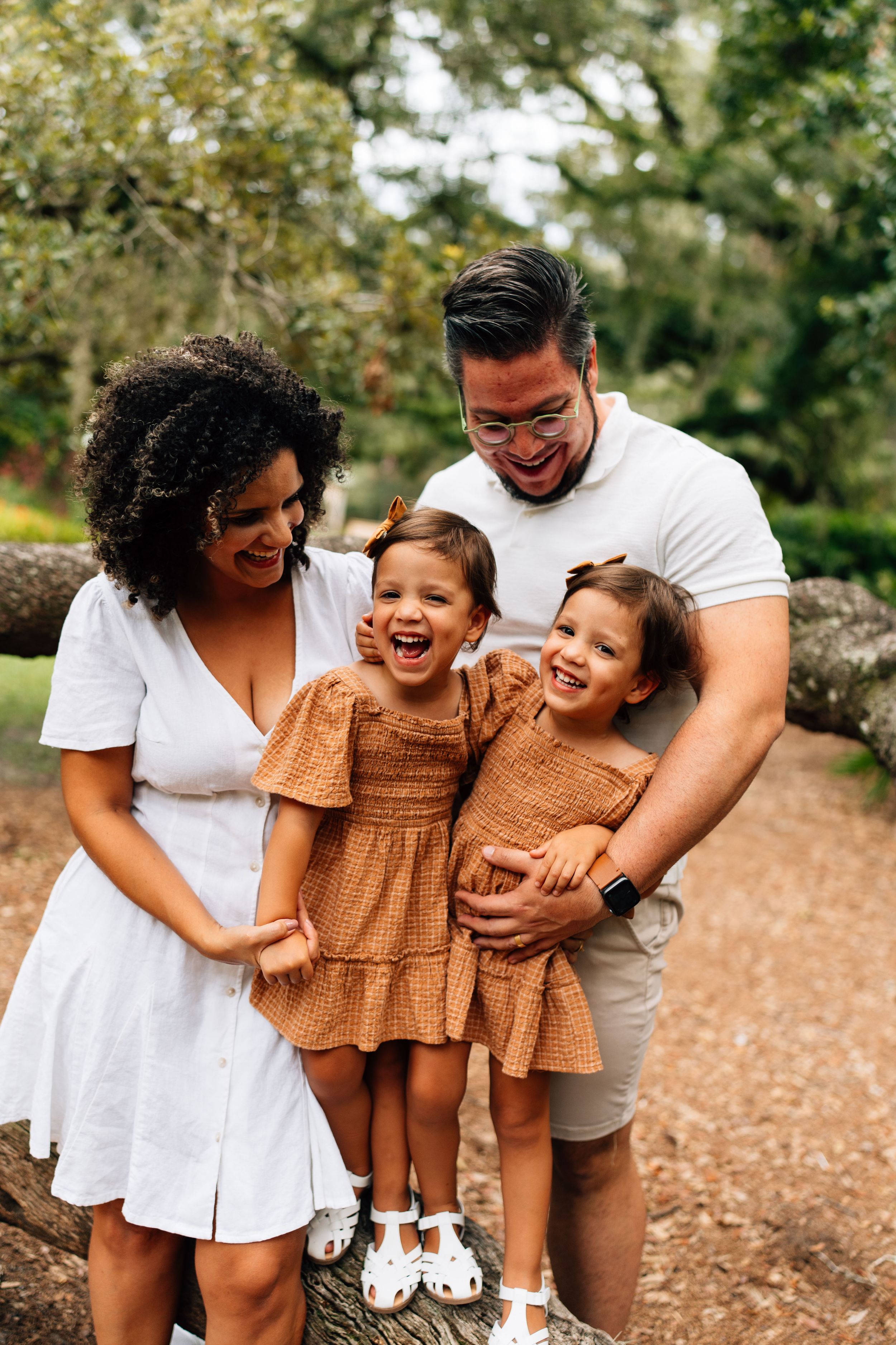 A joyful family plays and embraces outdoors on a trail in coordinated white and brown outfits during a photoshoot.