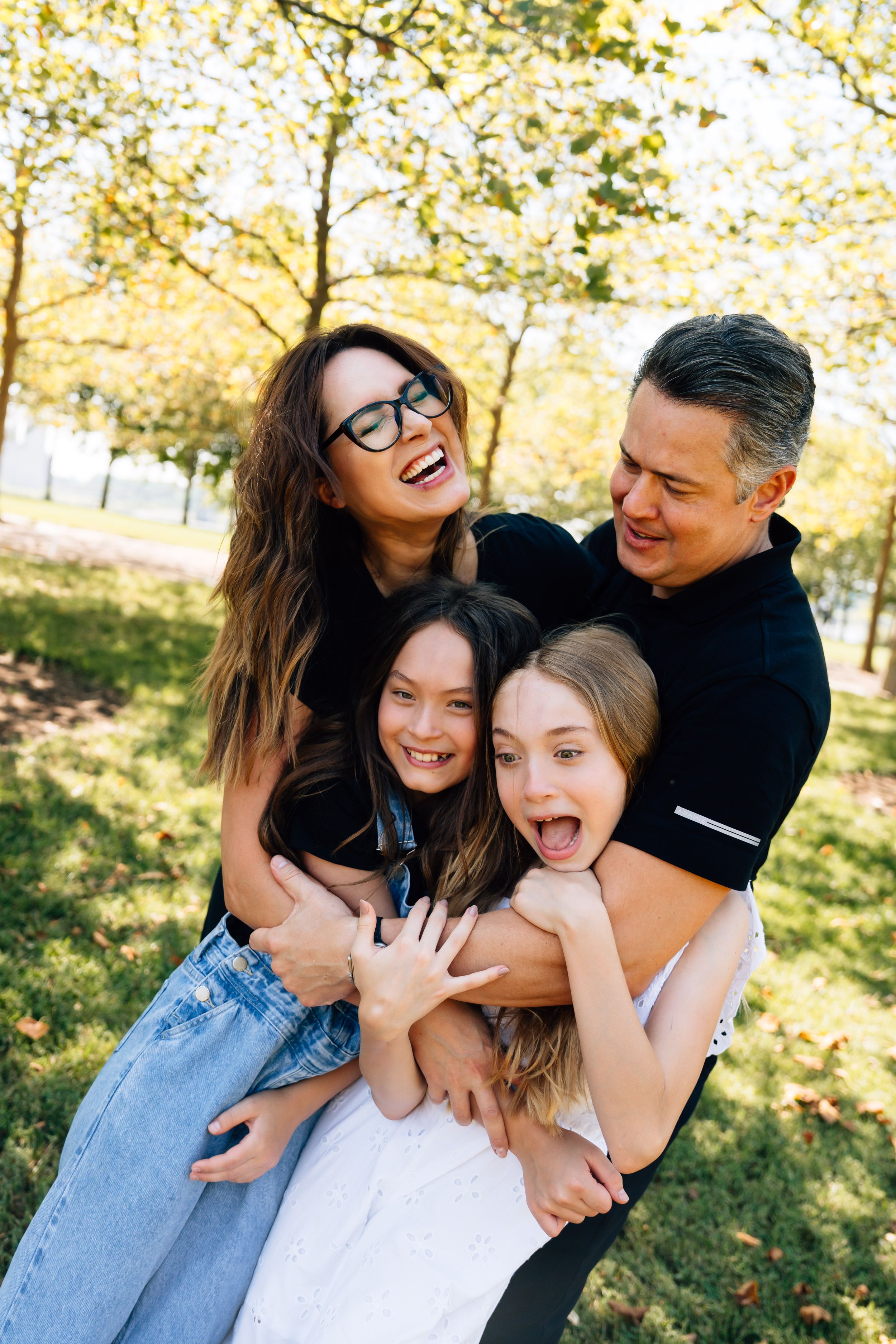 Multiple candid shots showing joyful laughter and embraces among a group in a sunny outdoor setting with autumn trees.