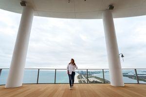 A panoramic view of a curved white architectural space with columns and glass windows overlooking an ocean landscape.