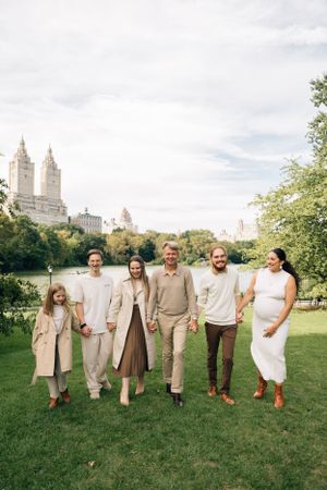 Group in neutral-toned outfits poses together on grass with Central Park West buildings in background.