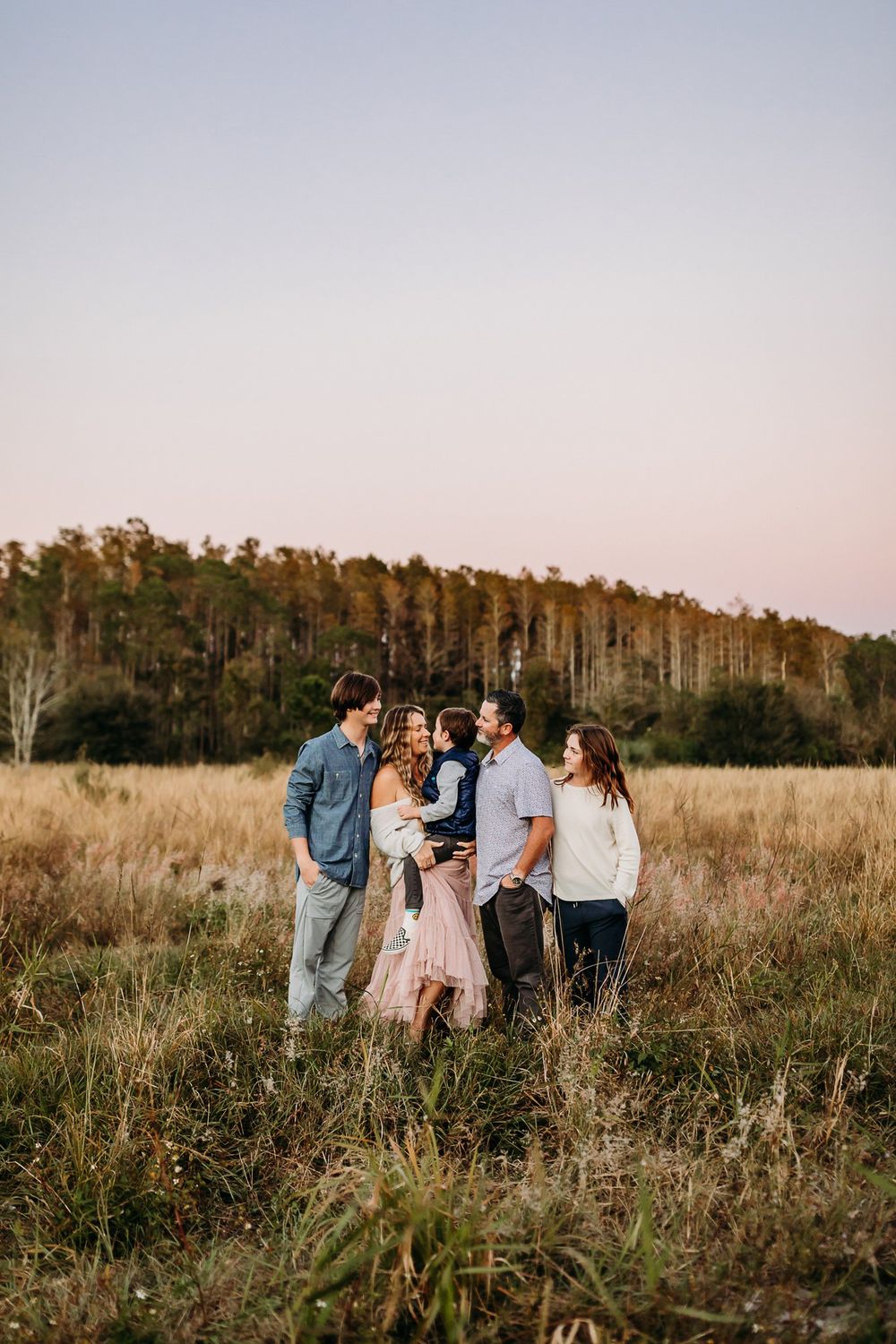 A group stands together in a golden autumn field at sunset as trees line the horizon in warm evening light.