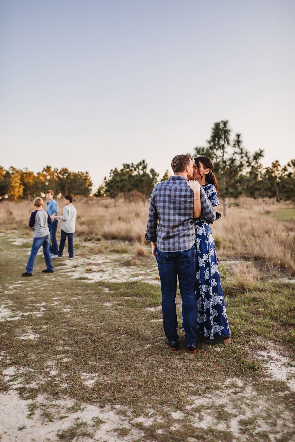 A couple wearing plaid and blue holds each other close while walking along a sandy path during golden hour sunset.