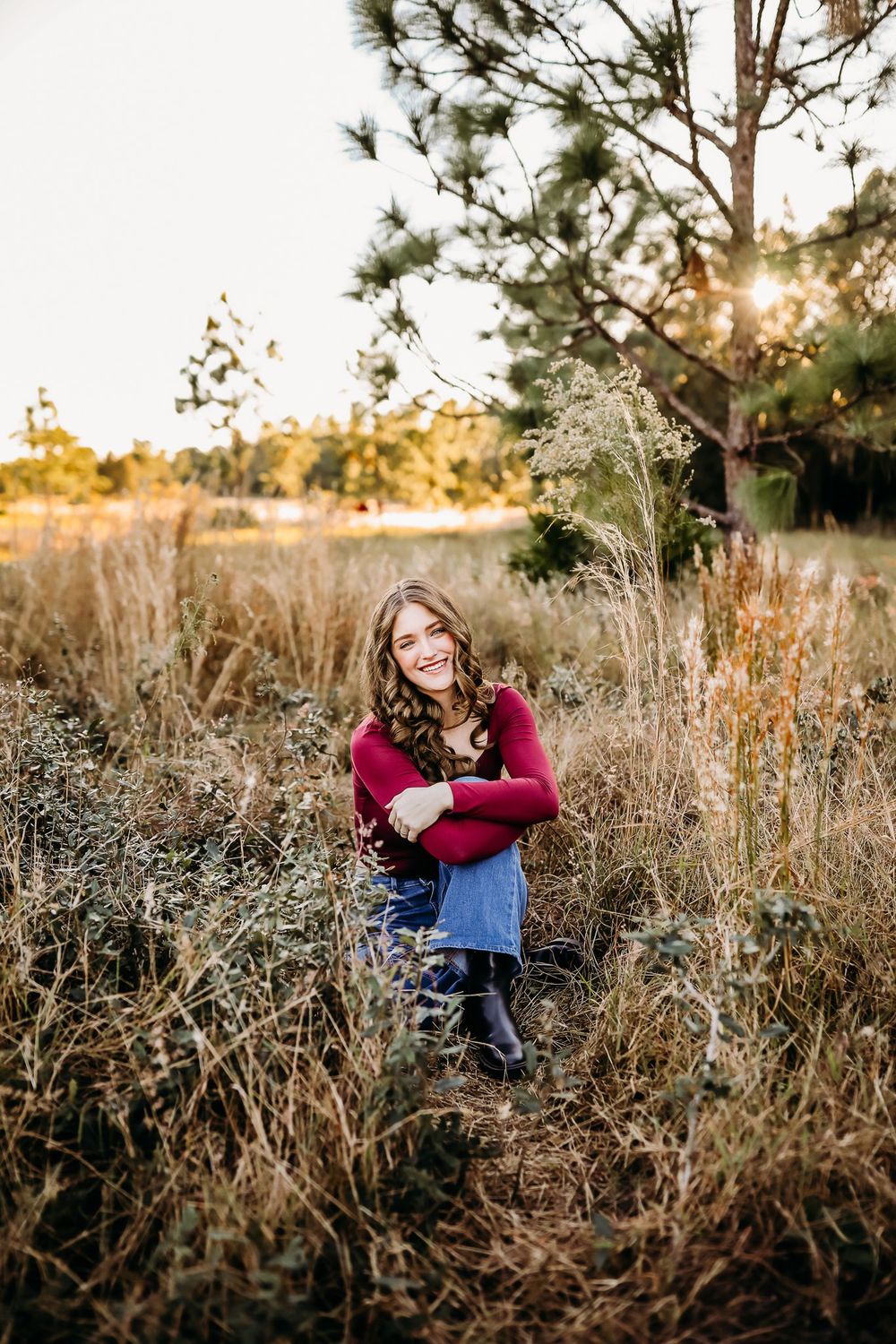 Golden sunlight illuminates dried grass and pine trees in a natural outdoor portrait session at golden hour.