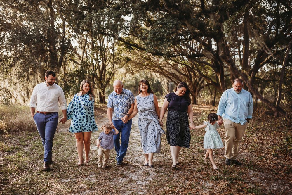 Extended family group walks together in a line on a wooded trail during golden hour sunset.