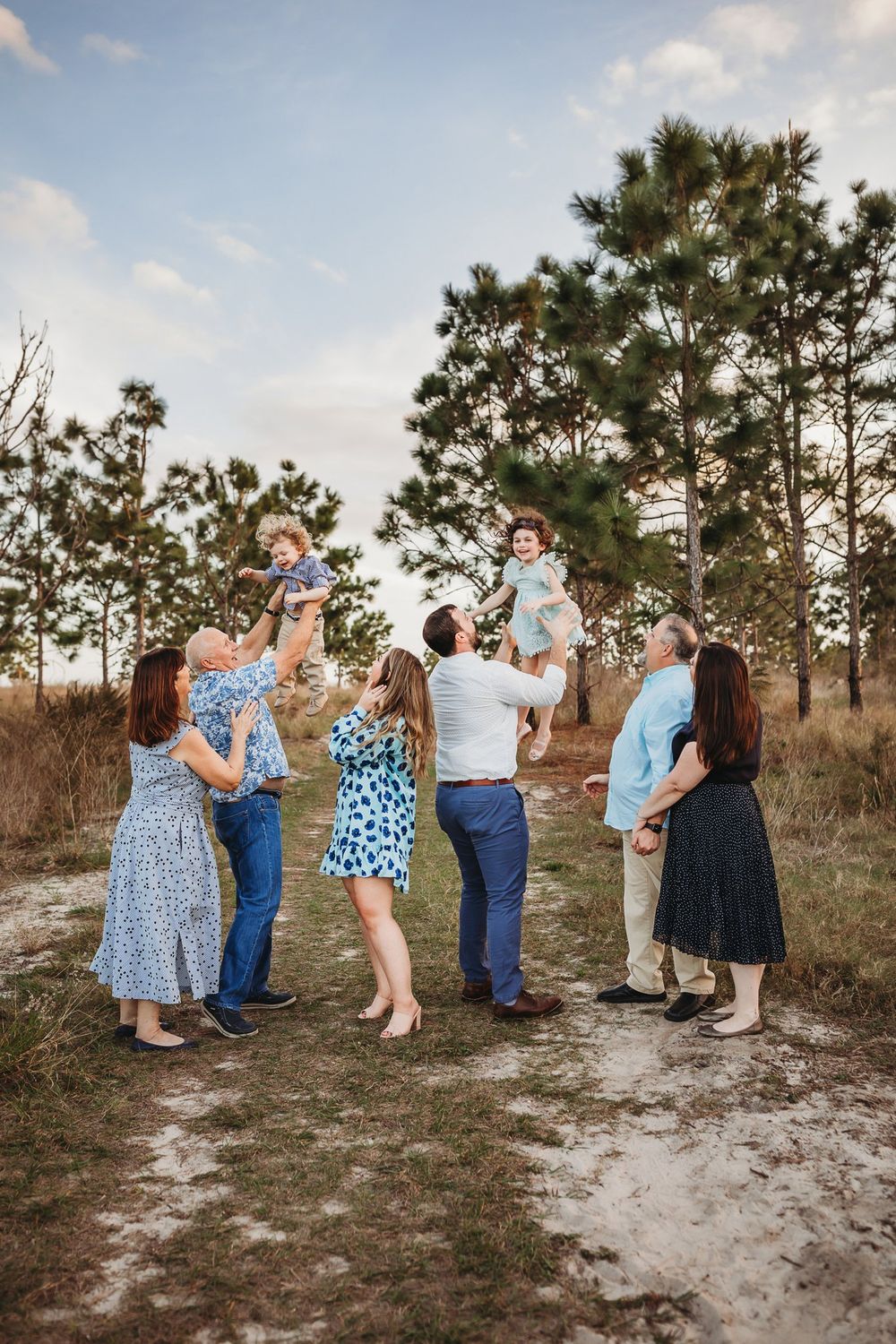 Group gathering in casual attire at a sandy clearing surrounded by pine trees during golden hour.