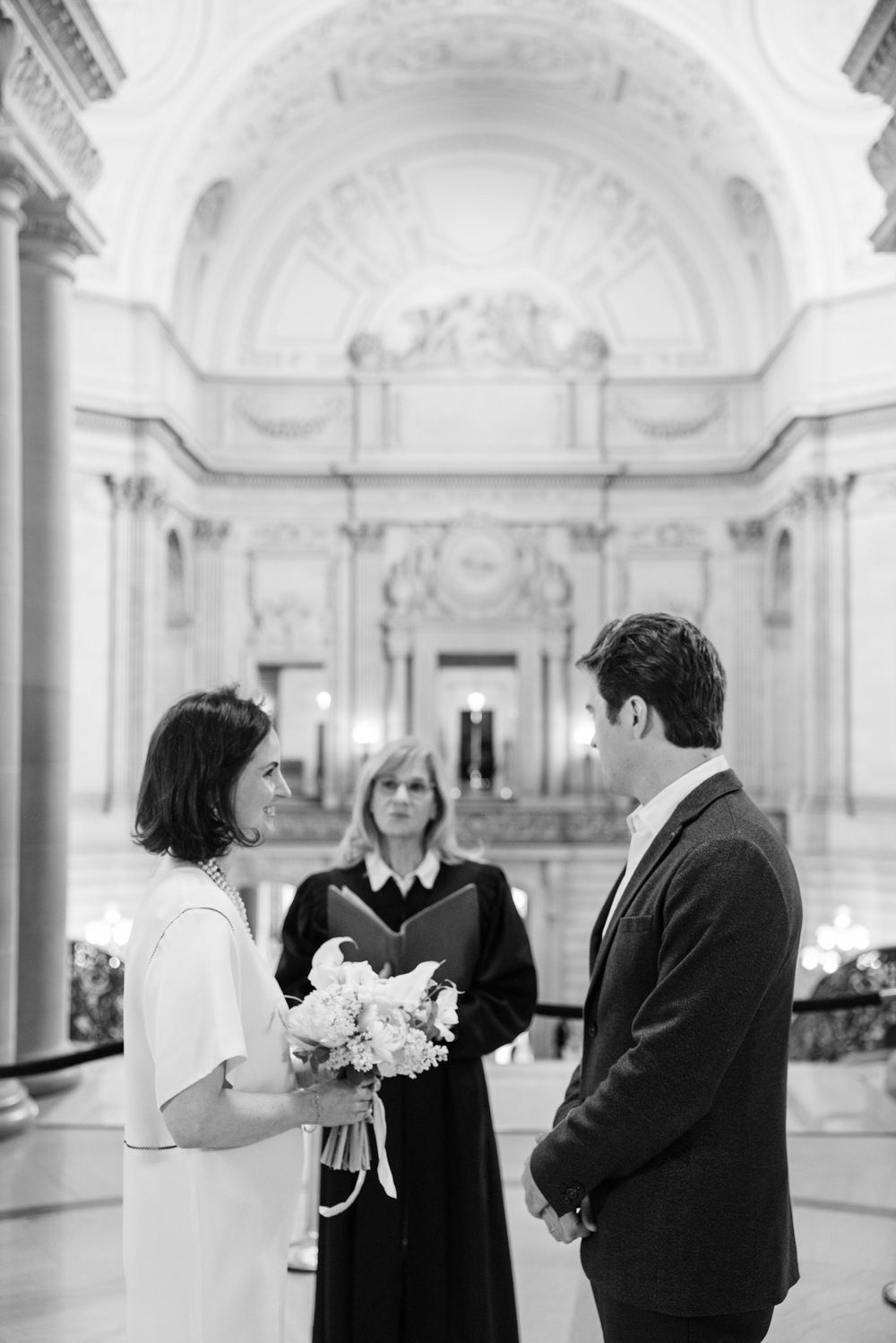 A series of black and white wedding photographs showing intimate moments between couples in an ornate white hallway.