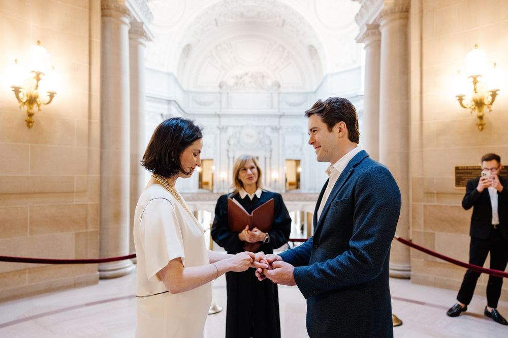 A couple exchanges vows during an intimate civil ceremony in an elegant marble hallway with classical architecture.