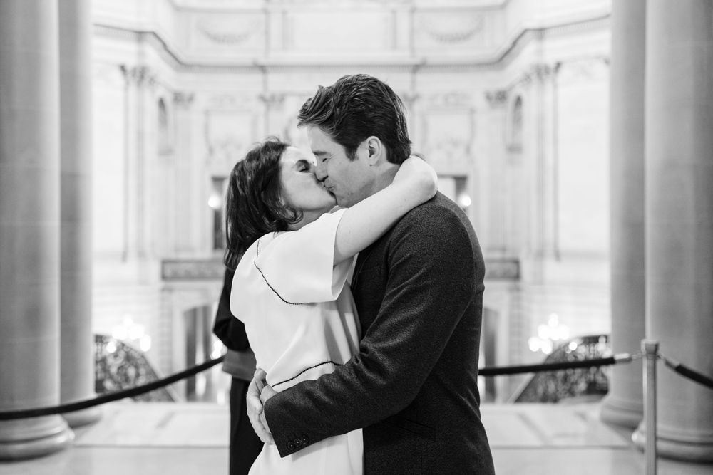 Black and white photos show a romantic couple embracing and kissing in an elegant hallway with white columns.