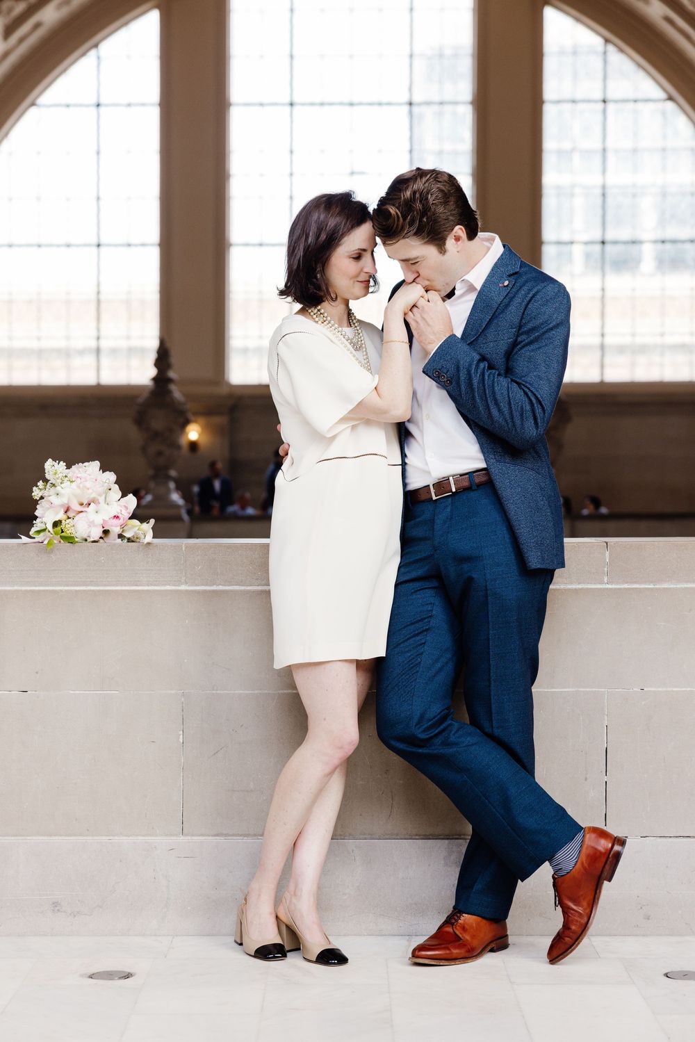 Romantic sequence of a couple in blue suit and white dress posing playfully by architectural windows.