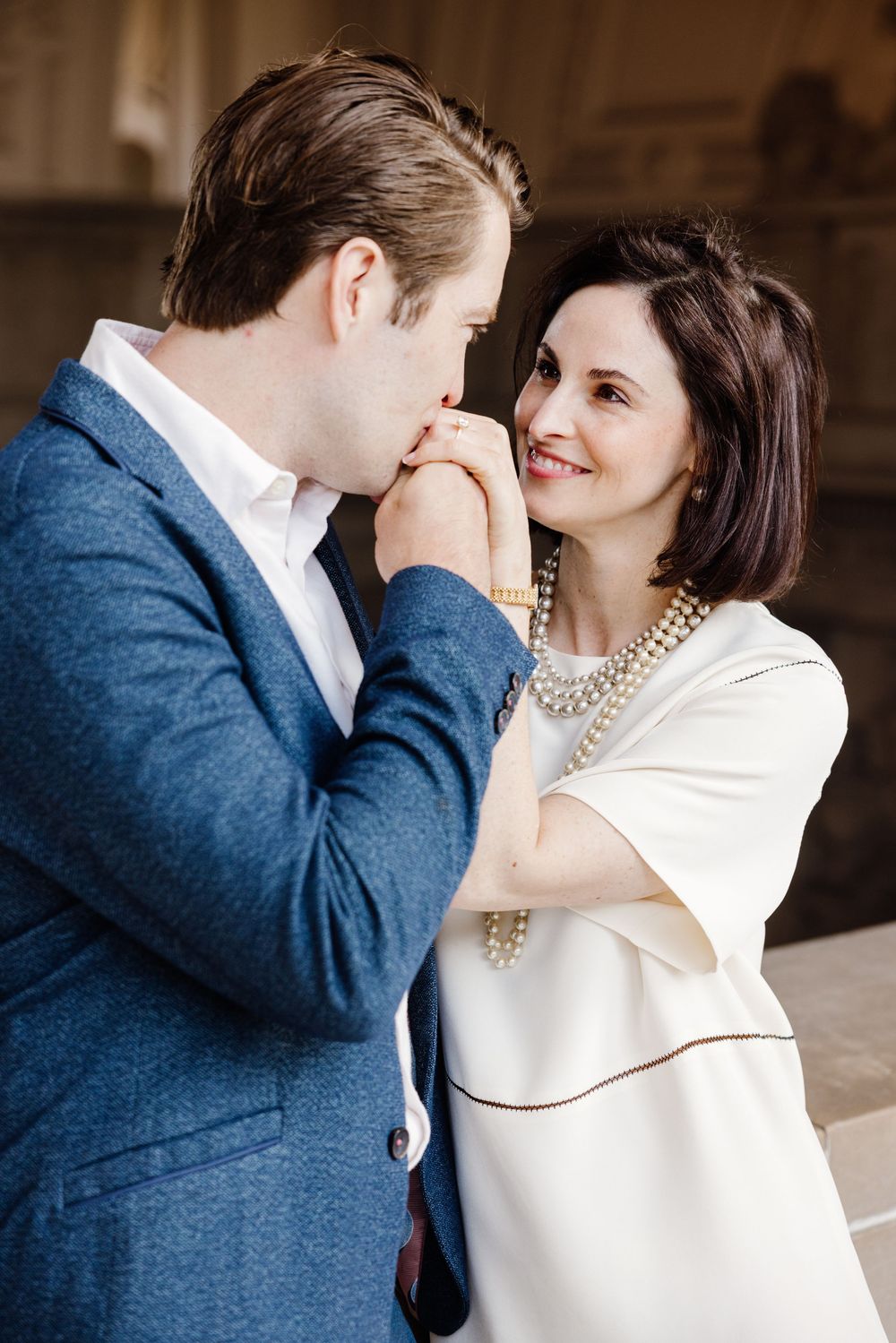 A couple shares an intimate moment in a romantic photoshoot, with him in navy and her in cream colored attire.