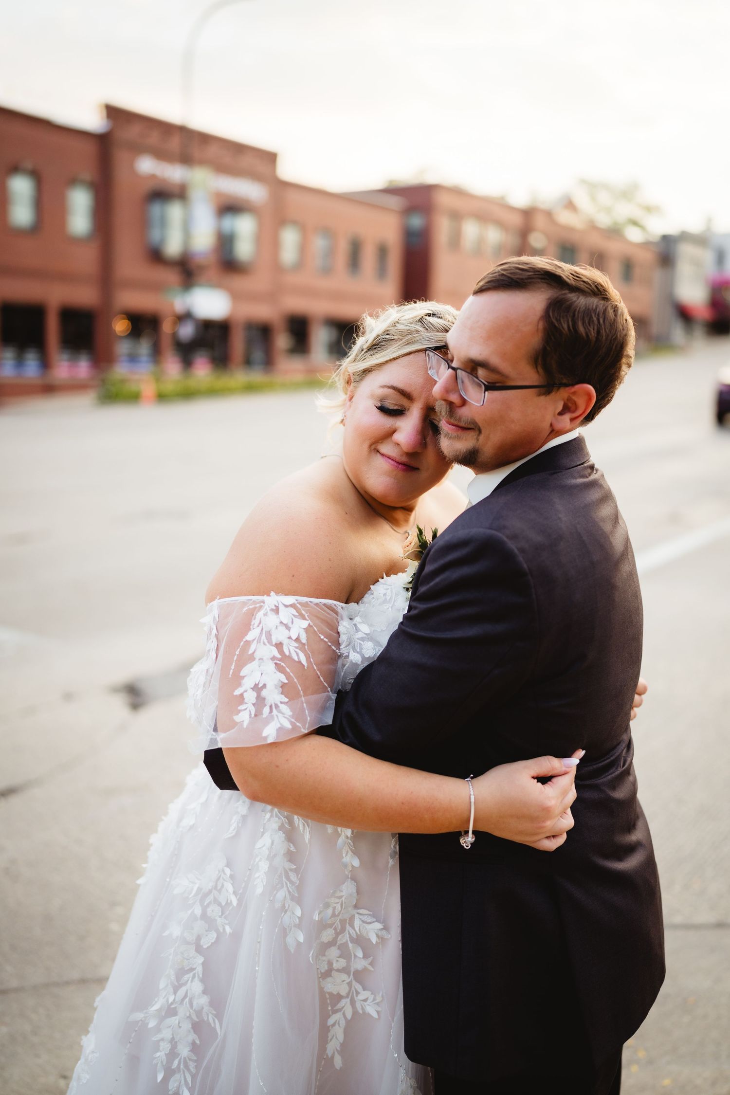 Newlywed couple embraces in a tender candid moment on their wedding day against red brick buildings.