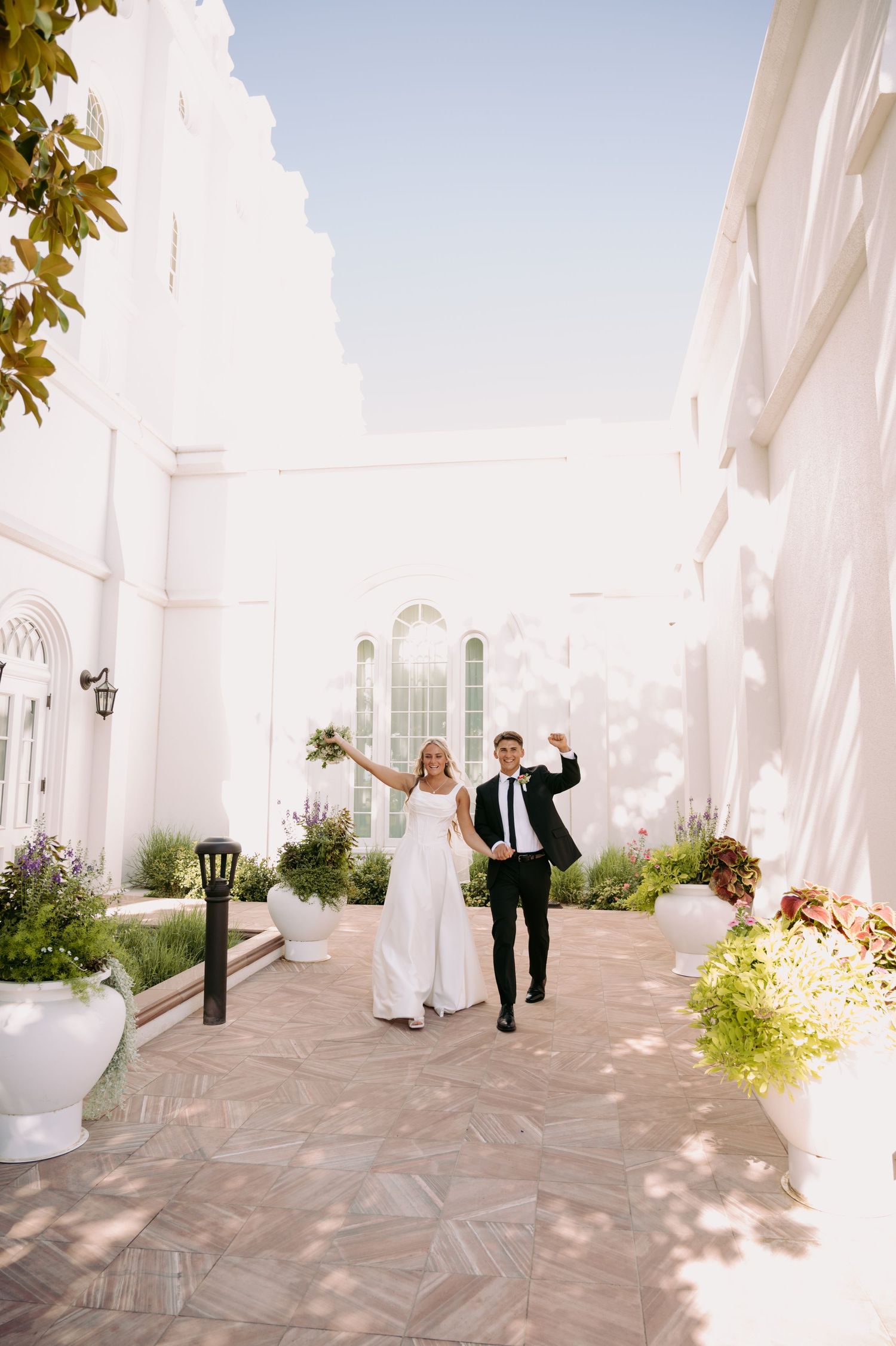 A couple poses playfully in a bright white hallway with elegant architecture and natural lighting.