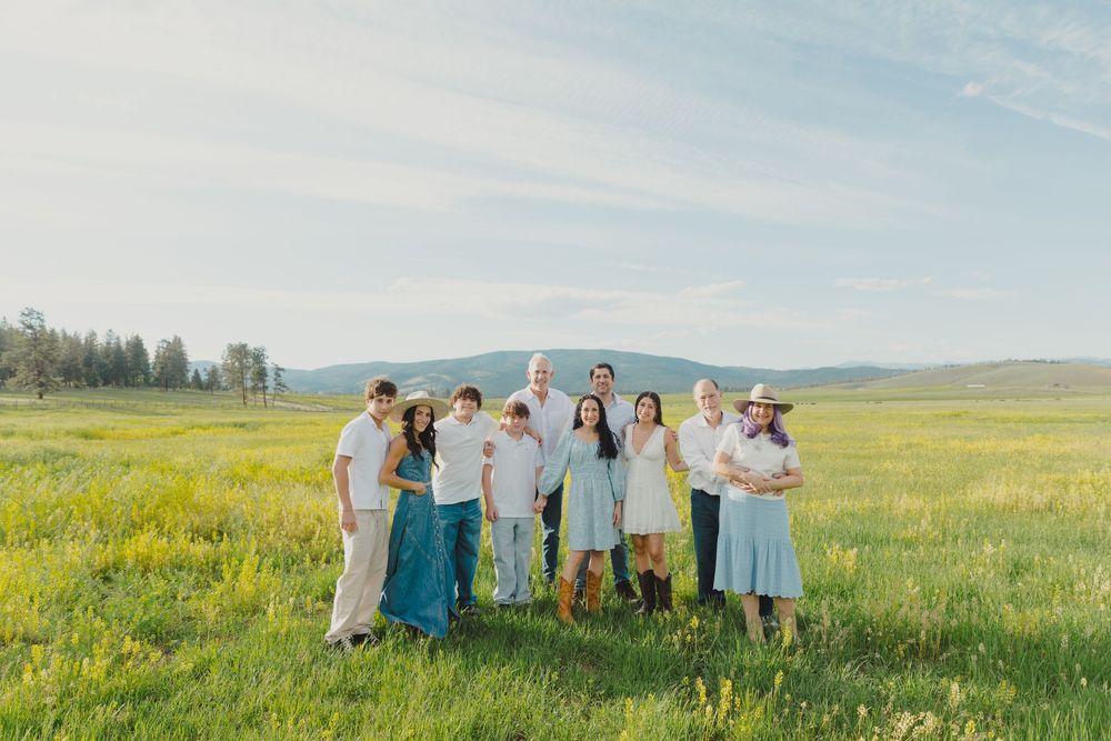 Large family group smiling together in a lush green meadow under a bright blue sky during a sunny day.