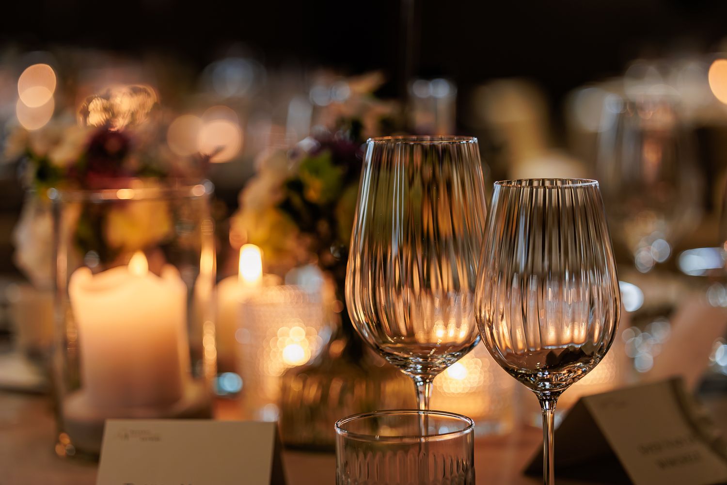Elegant wine glasses and glowing candles create a romantic dining atmosphere in a dimly lit restaurant setting.