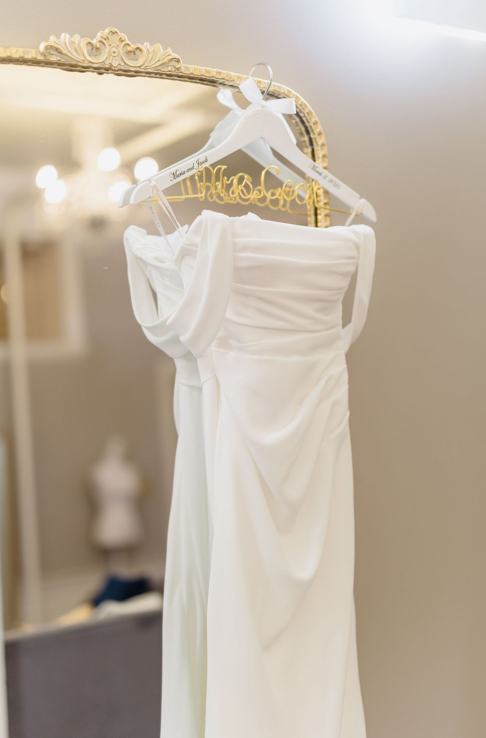 White wedding gowns hanging on elegant gold hangers against a light neutral wall.