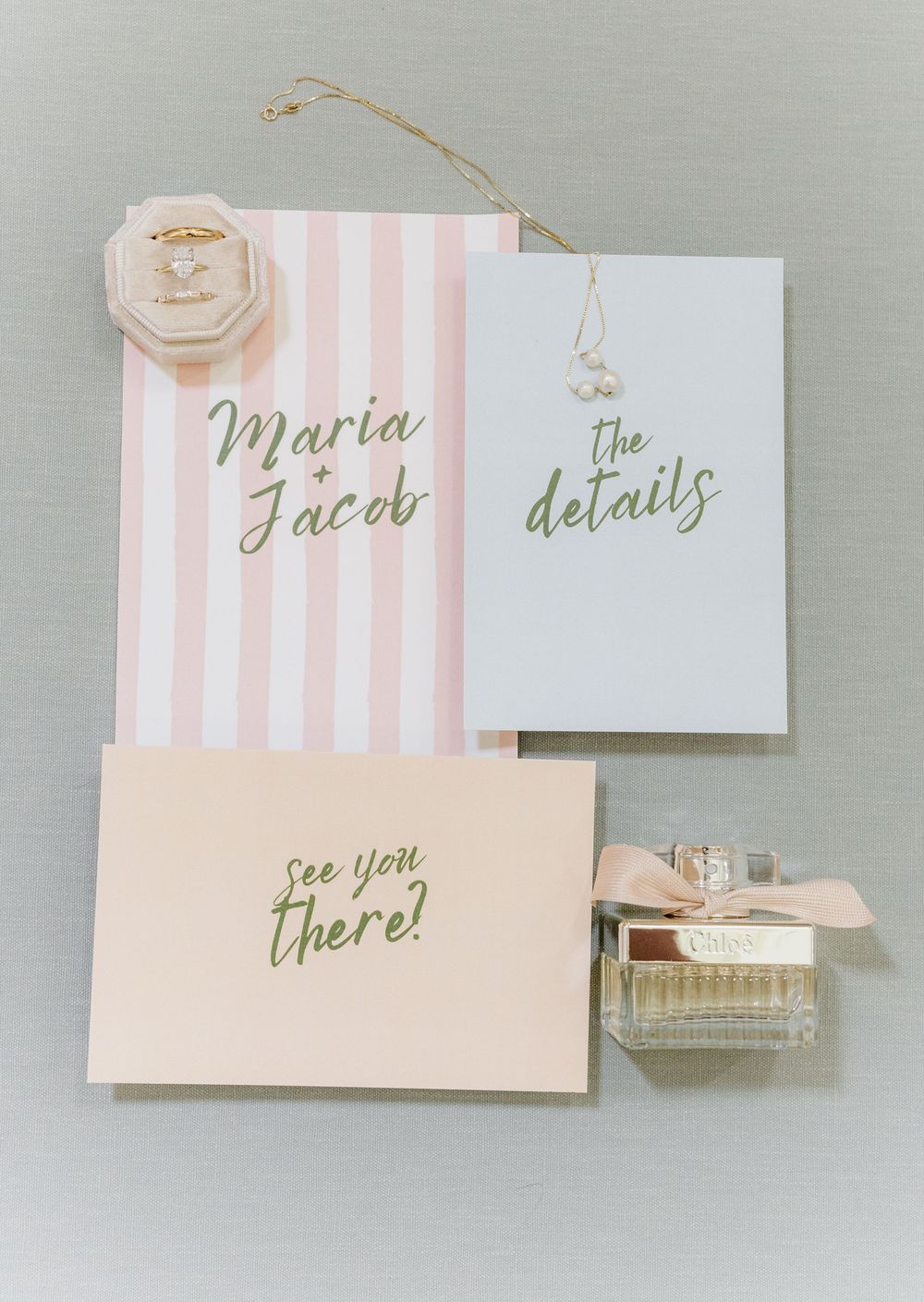Pink and white striped wedding stationery cards with delicate gold calligraphy laid out on a gray surface.