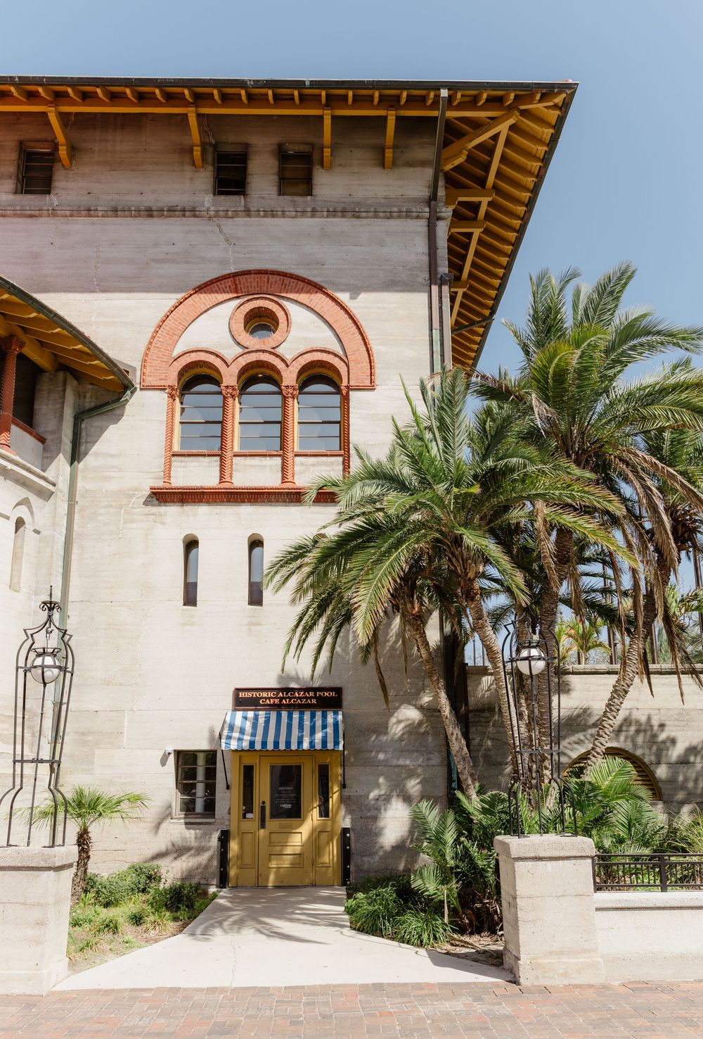 Elegant Mediterranean-style building exterior with white stone walls, arched windows, and palm trees lining the courtyard.