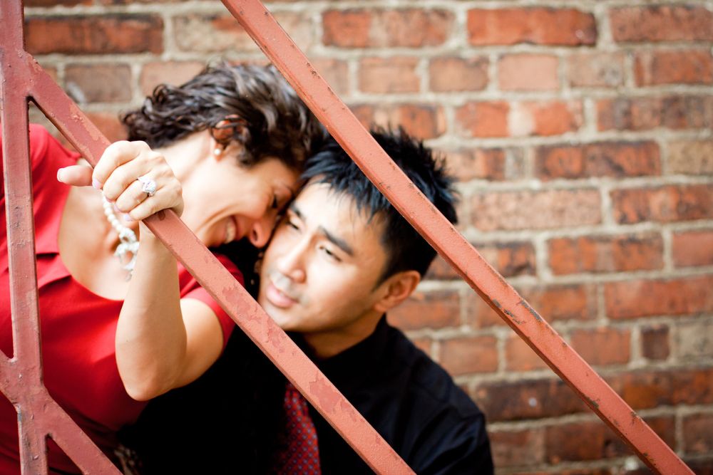 A romantic moment shared against a rustic brick wall with red metal railings.during their engagement session