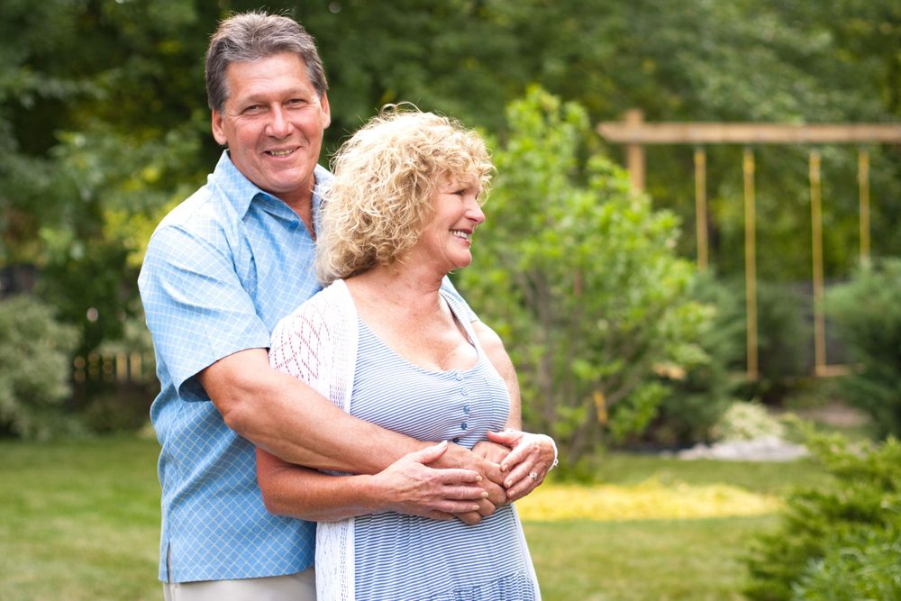 A mature couple embracing in a sunny garden setting.