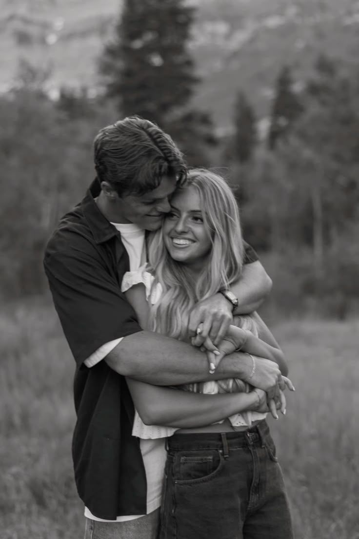 A couple in white and neutral outfits walks together through a grassy field in a moody black and white photograph.