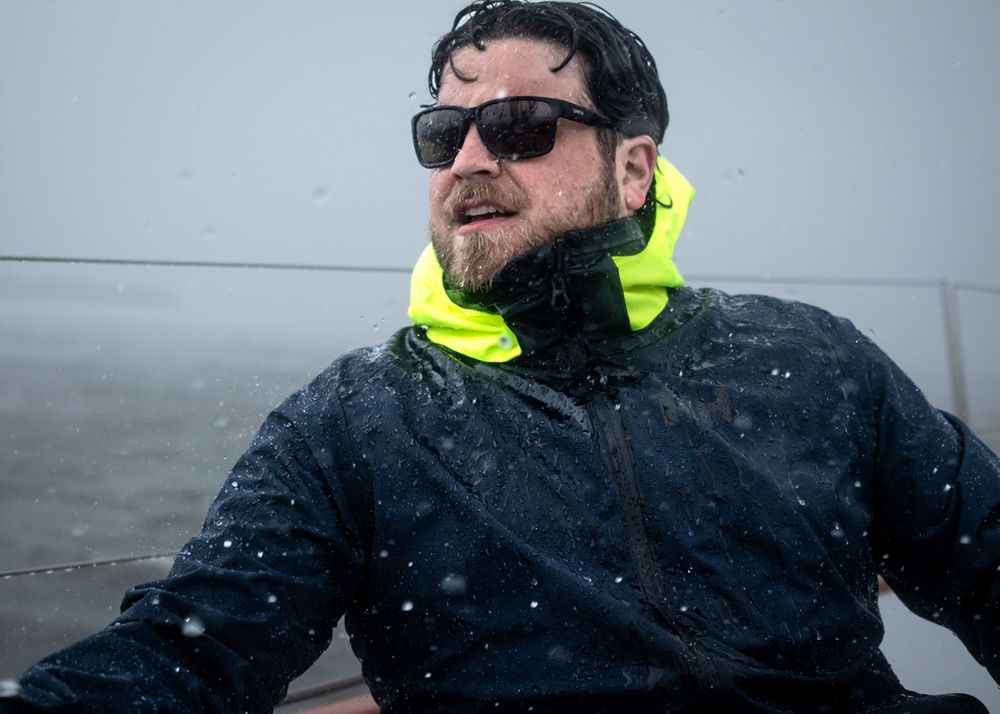 Sailor wears jacket during rainstorm for sailing brand photography photoshoot.
