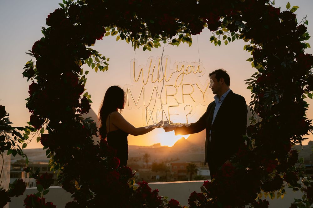 Group of silhouetted people stand in front of a golden sunset sky with tree branches framing the scene.