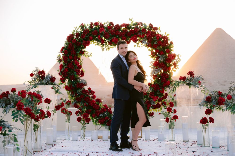 A series of white wedding arches decorated with cascading red roses and floral arrangements at sunset.