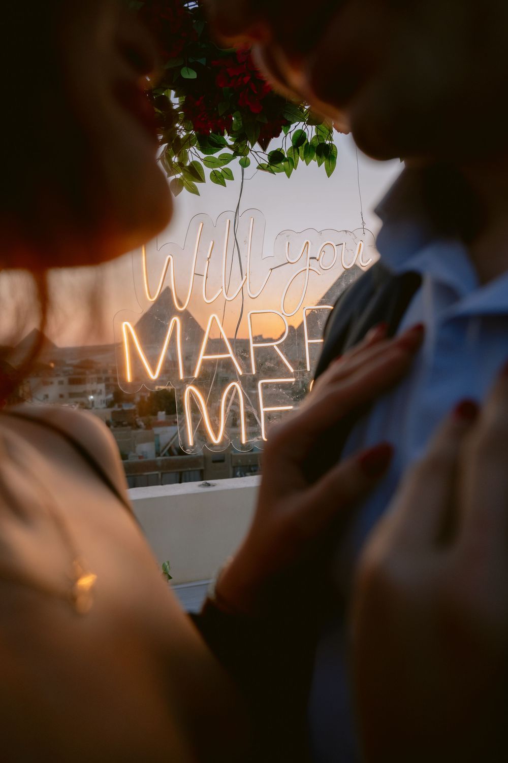 Illuminated marriage proposal sign with neon letters spelling out a romantic message against a dusky background.
