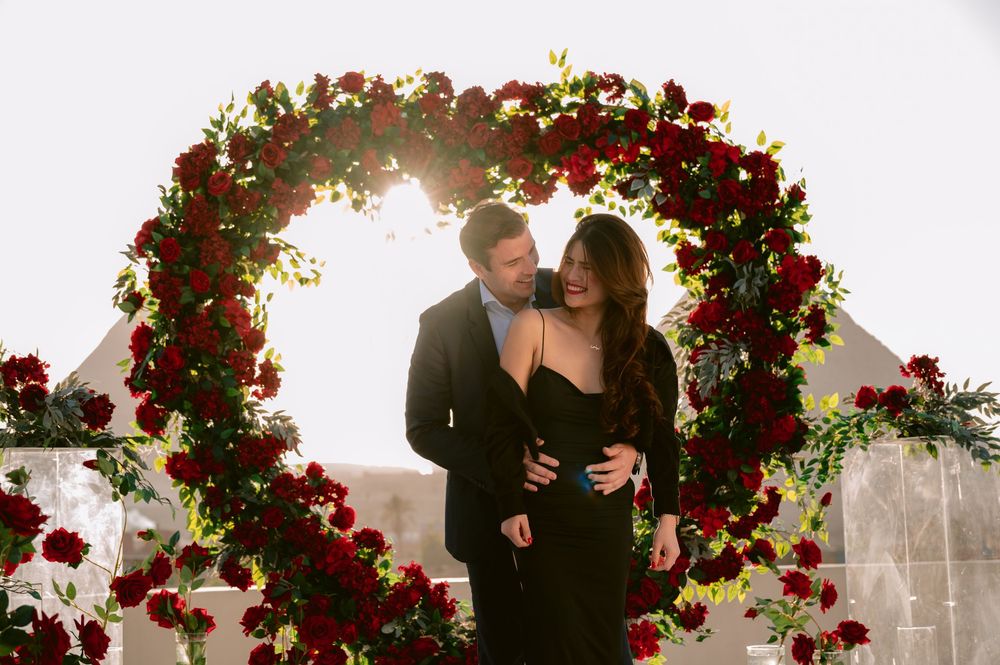 Couple sharing an intimate moment under an arch decorated with red roses at sunset.