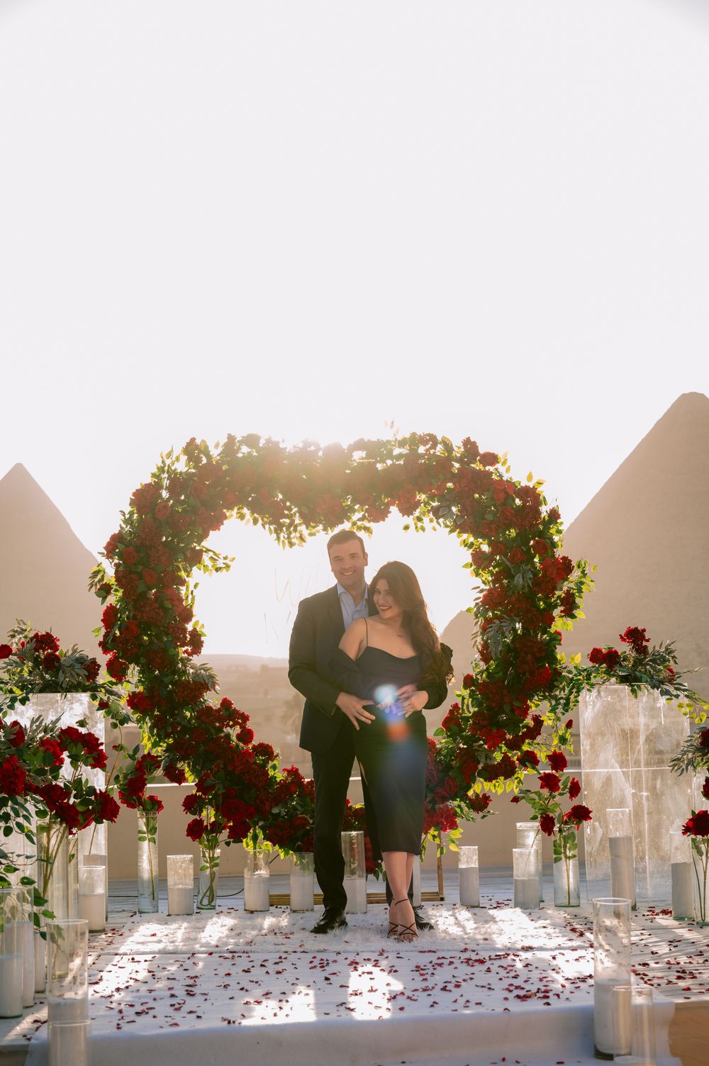Love blooms under a romantic floral archway as two figures dance in the sunlit glow of their wedding moment.