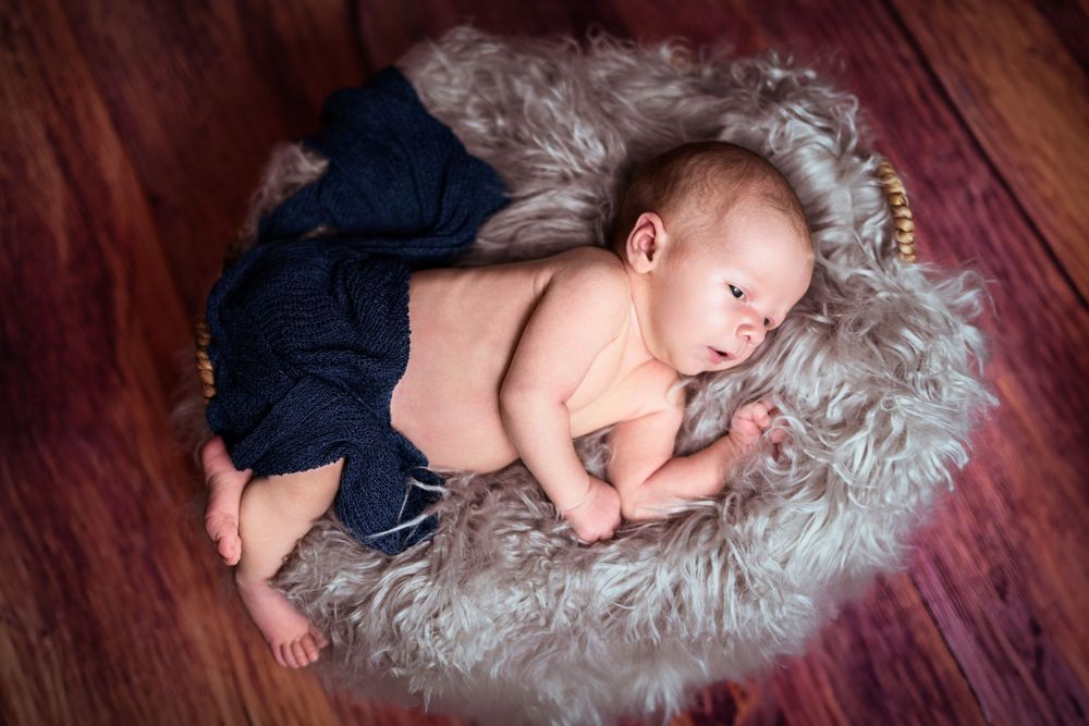 Newborn in navy outfit sleeping peacefully on gray fur rug.