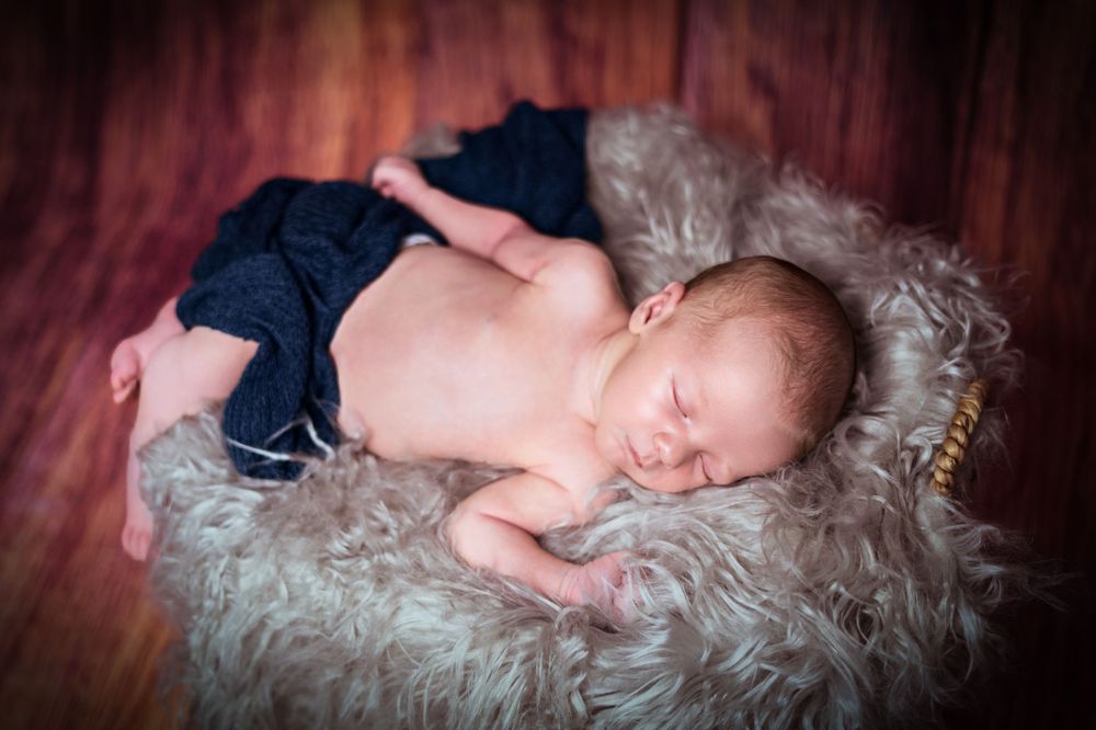 Sleeping newborn dressed in navy outfit on textured gray fur backdrop.